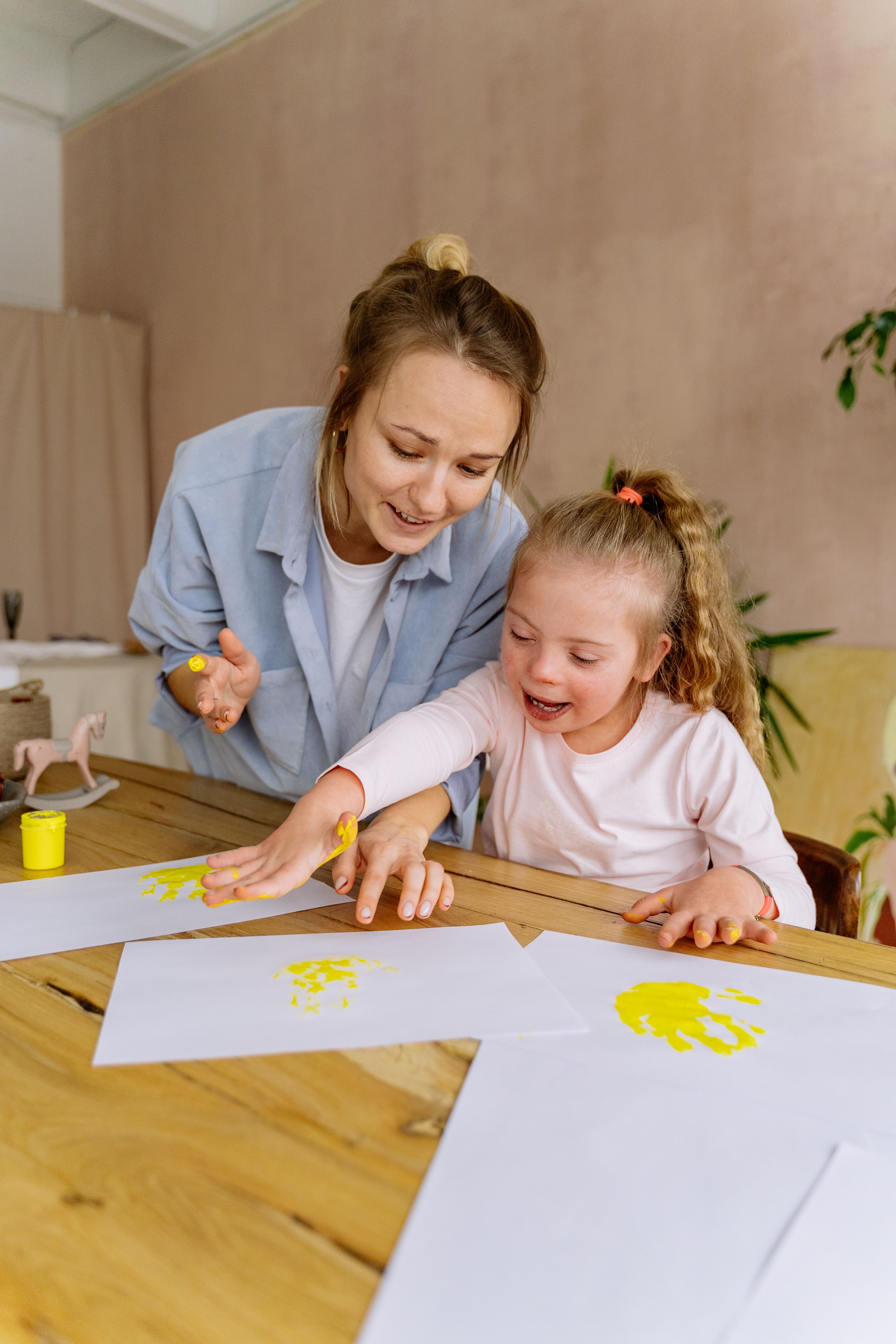 A therapist and a smiling child making handprint art together during a session